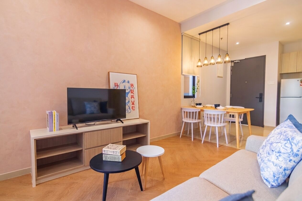 A modern living room with a flat-screen TV, a dining area with a table and chairs, and a kitchen in the background.