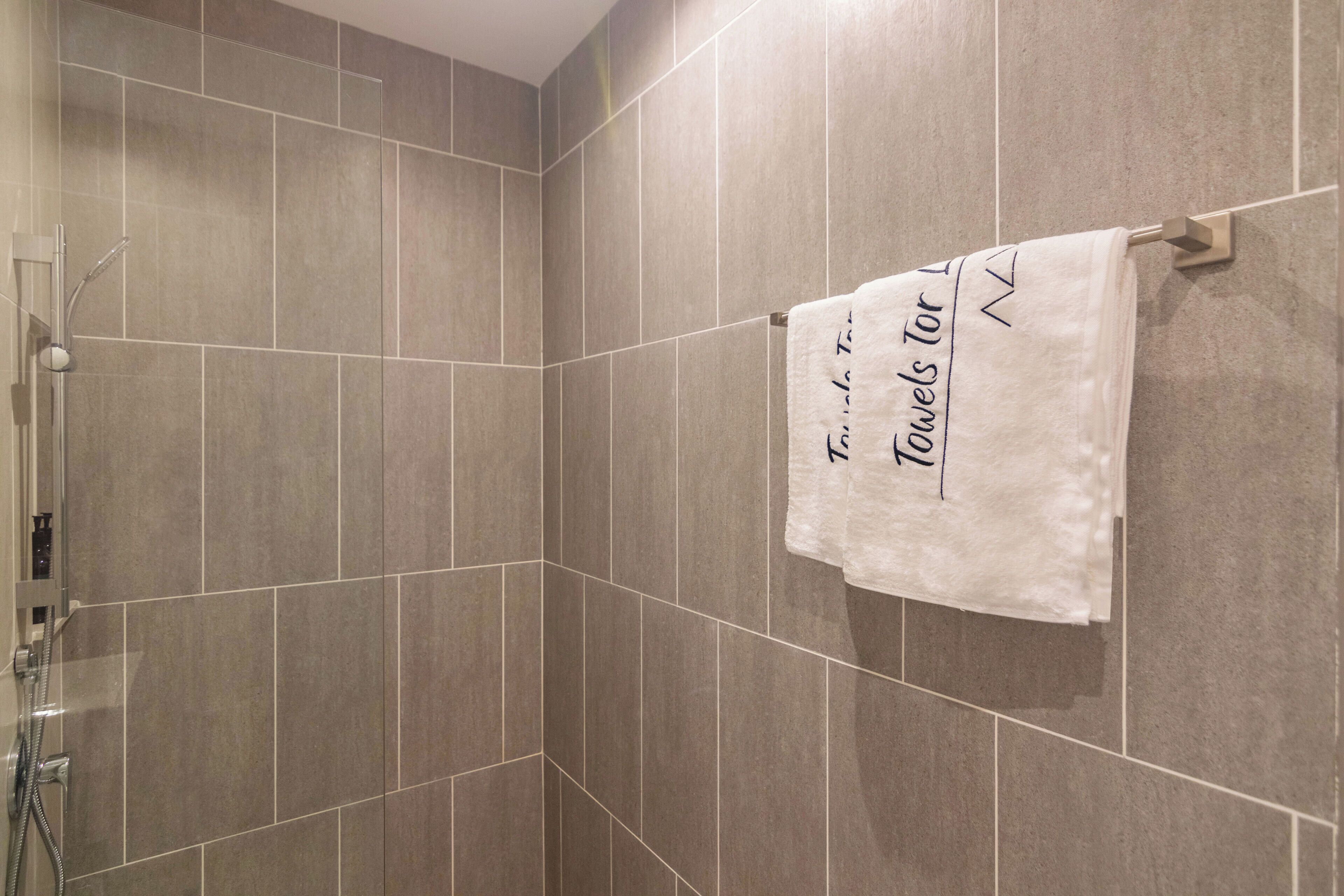 A bathroom with grey tiles, a towel rack with a towel, and a shower area.