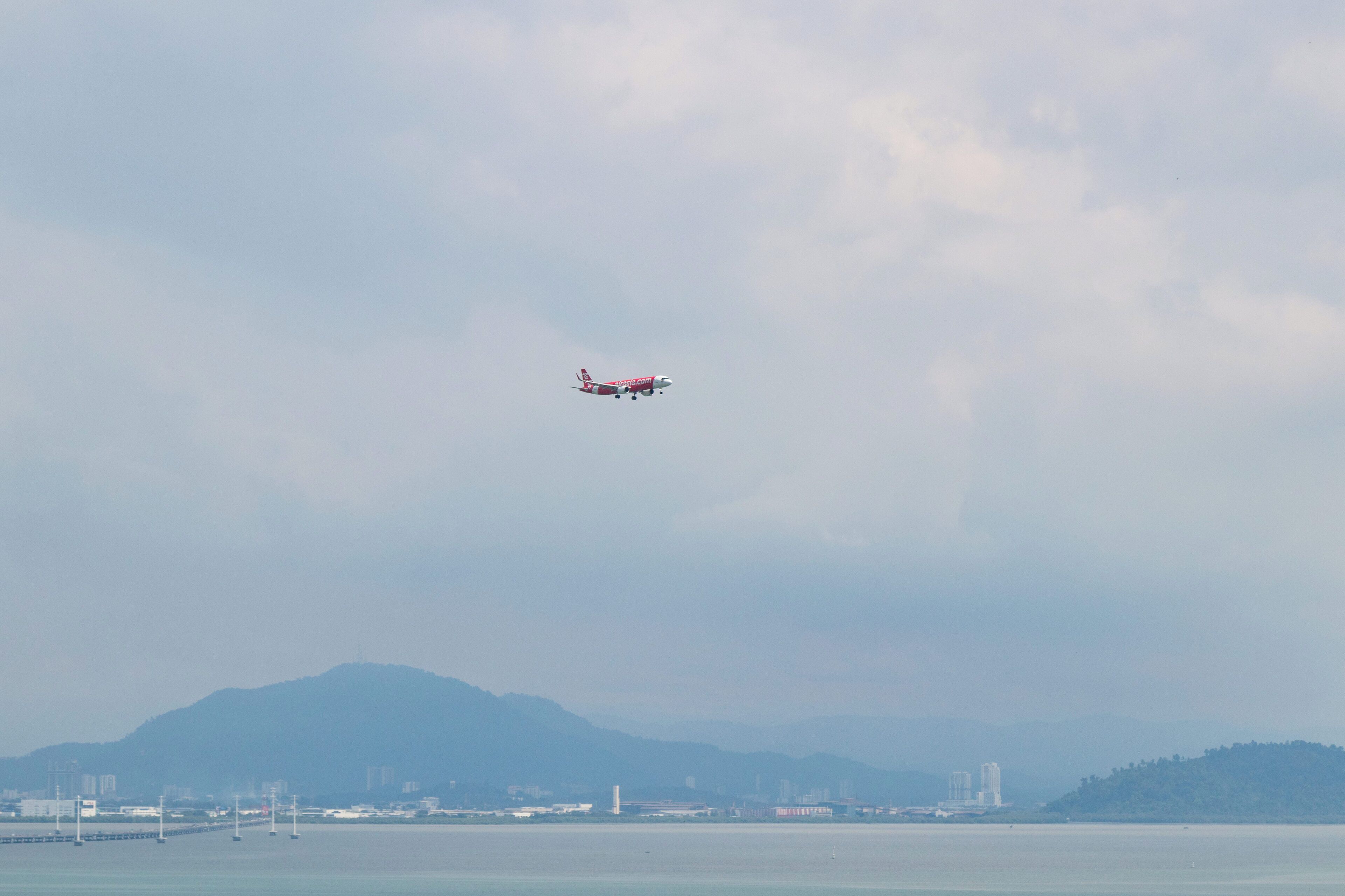 An airplane flying over a body of water with a cityscape and mountains in the background.