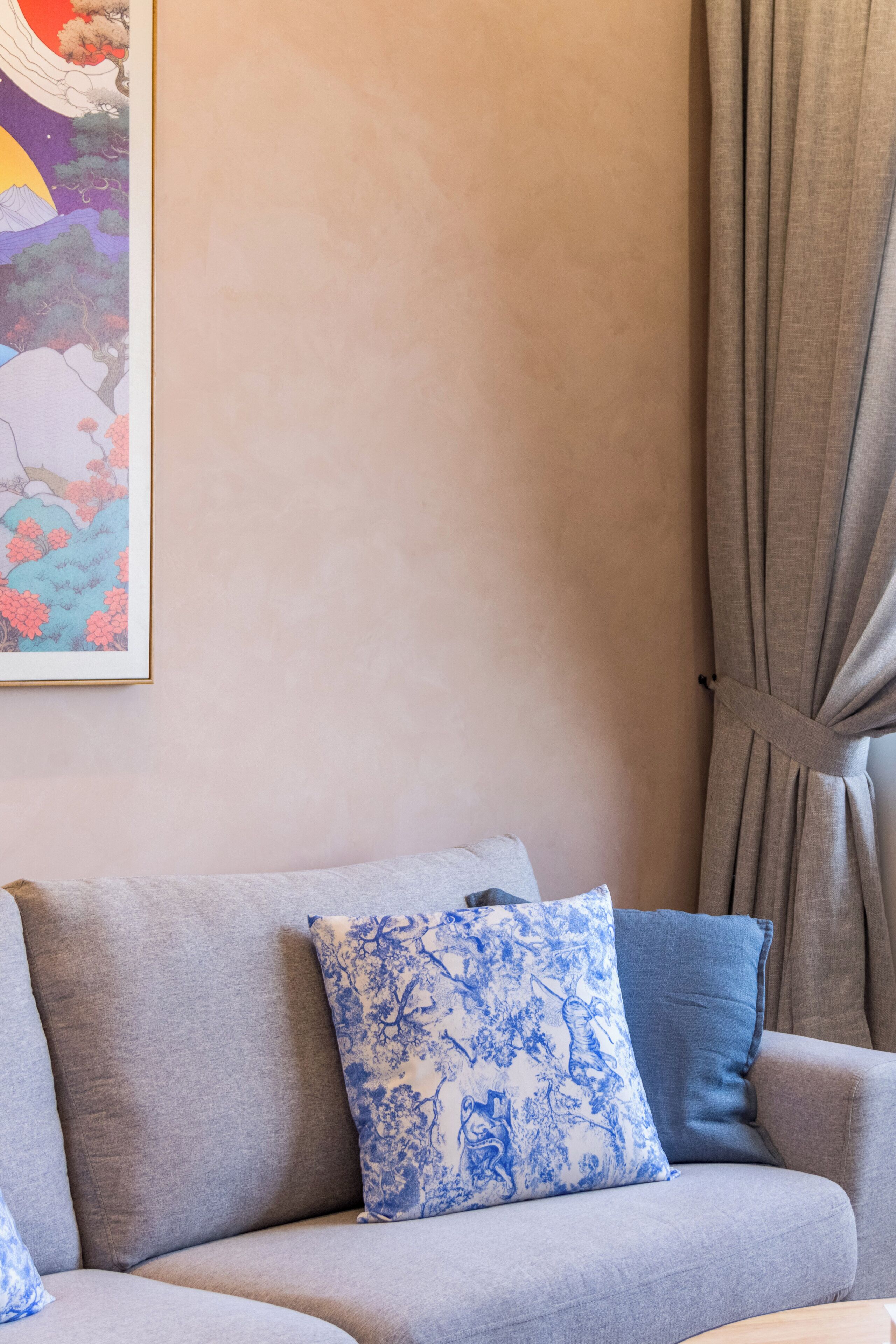 A living room with a grey sofa, blue patterned pillows, and a framed artwork on the wall.