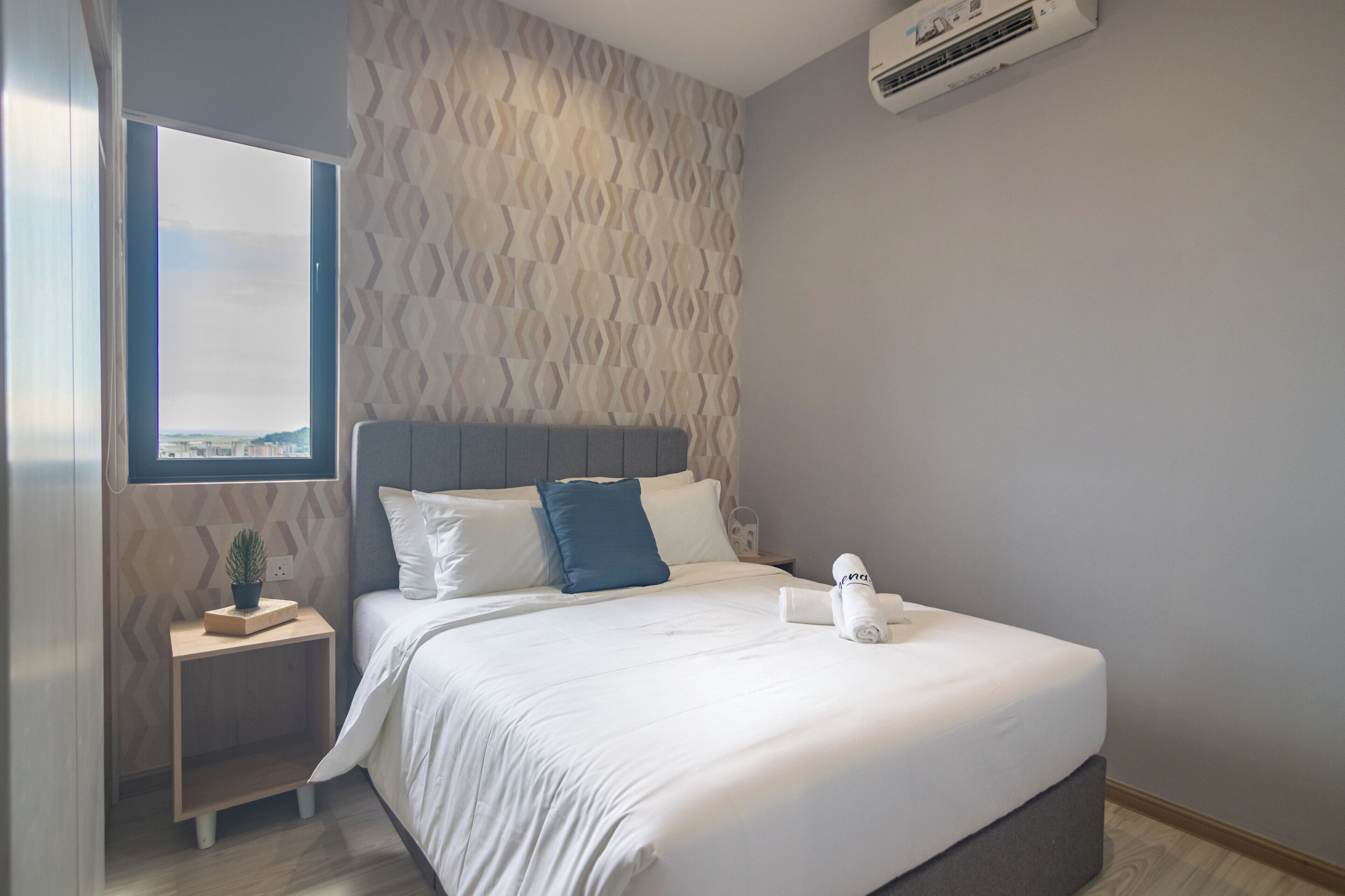 Ett modernt hotellrum med en stor säng, ett litet nattduksbord med en växt, ett fönster med utsikt och en luftkonditioneringsanläggning på väggen.