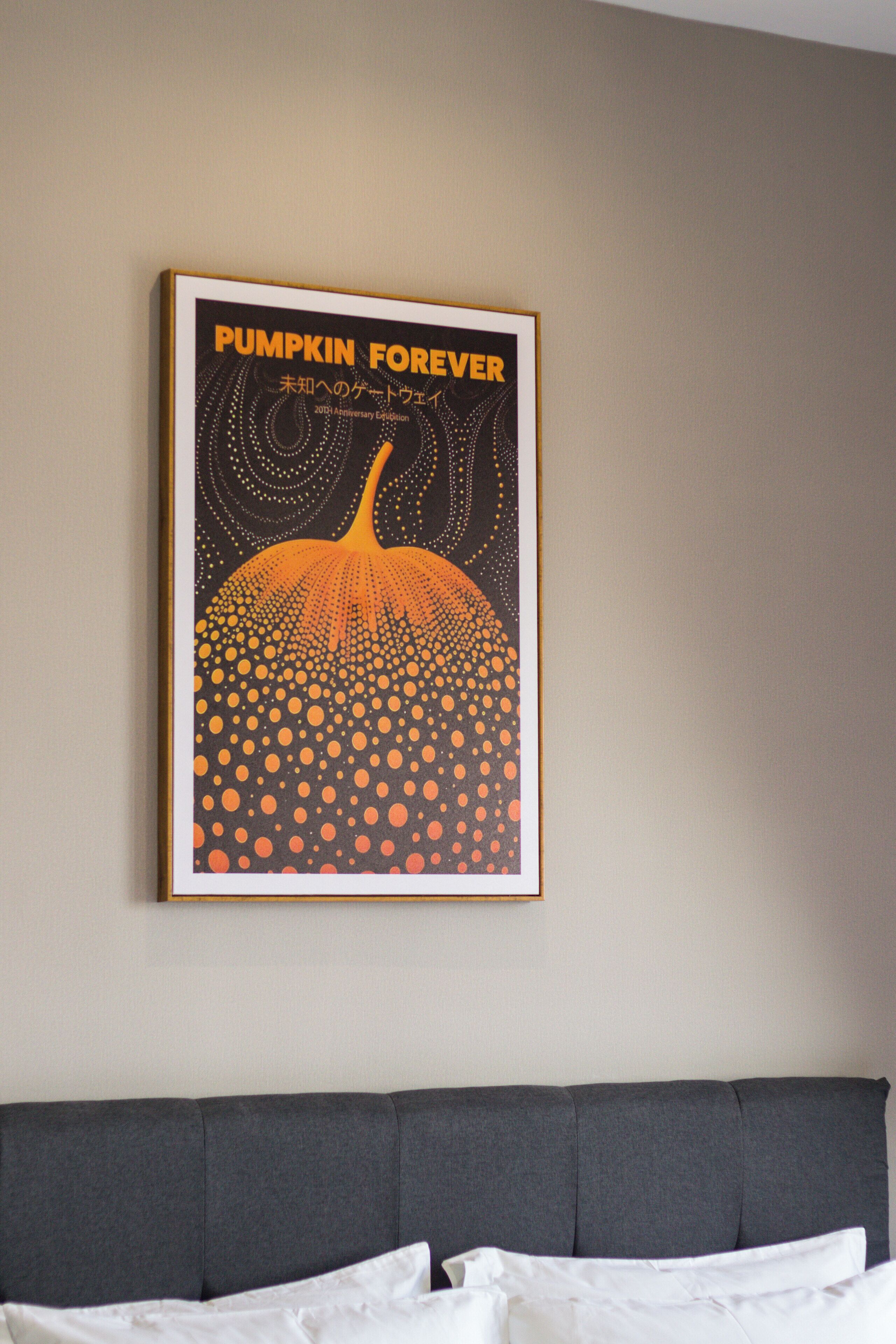 Una obra de arte enmarcada titulada 'Pumpkin Forever' sobre una pared, encima de un sofá gris.