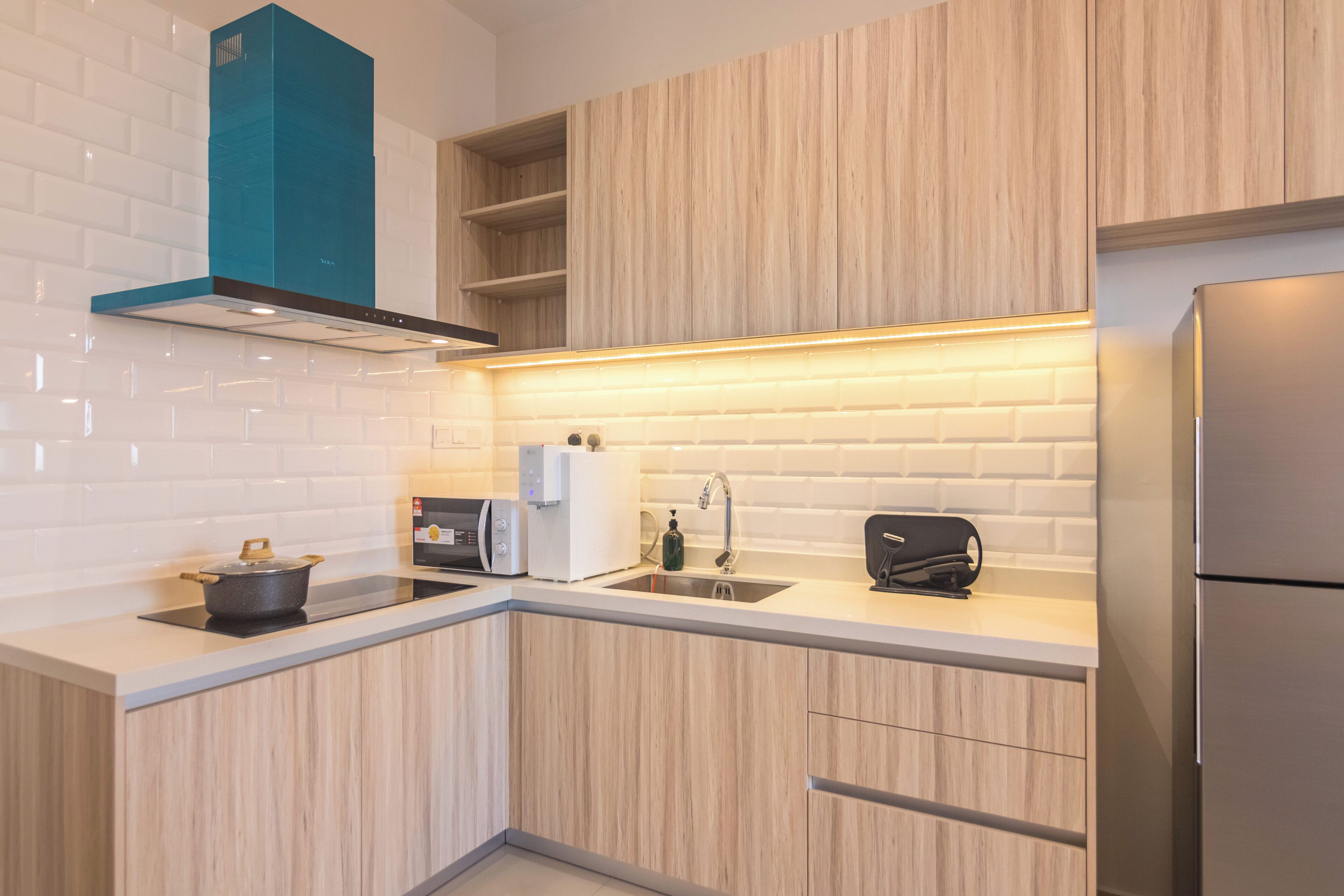 A modern kitchen with wooden cabinets, a built-in oven, a sink, and a stainless steel refrigerator.