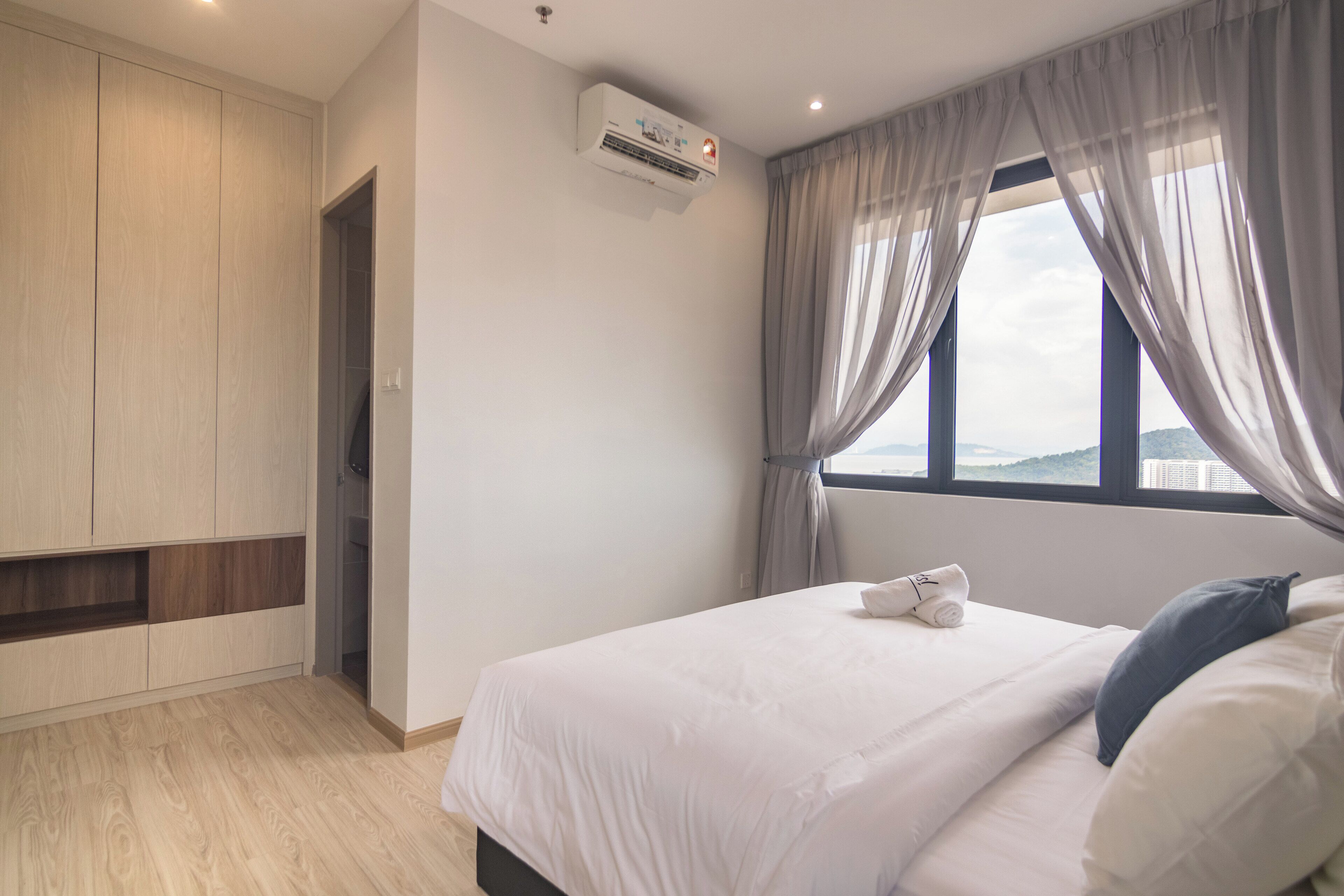 A bedroom with a bed, a wardrobe, an air conditioning unit, a window with curtains, and a view of the outdoors.