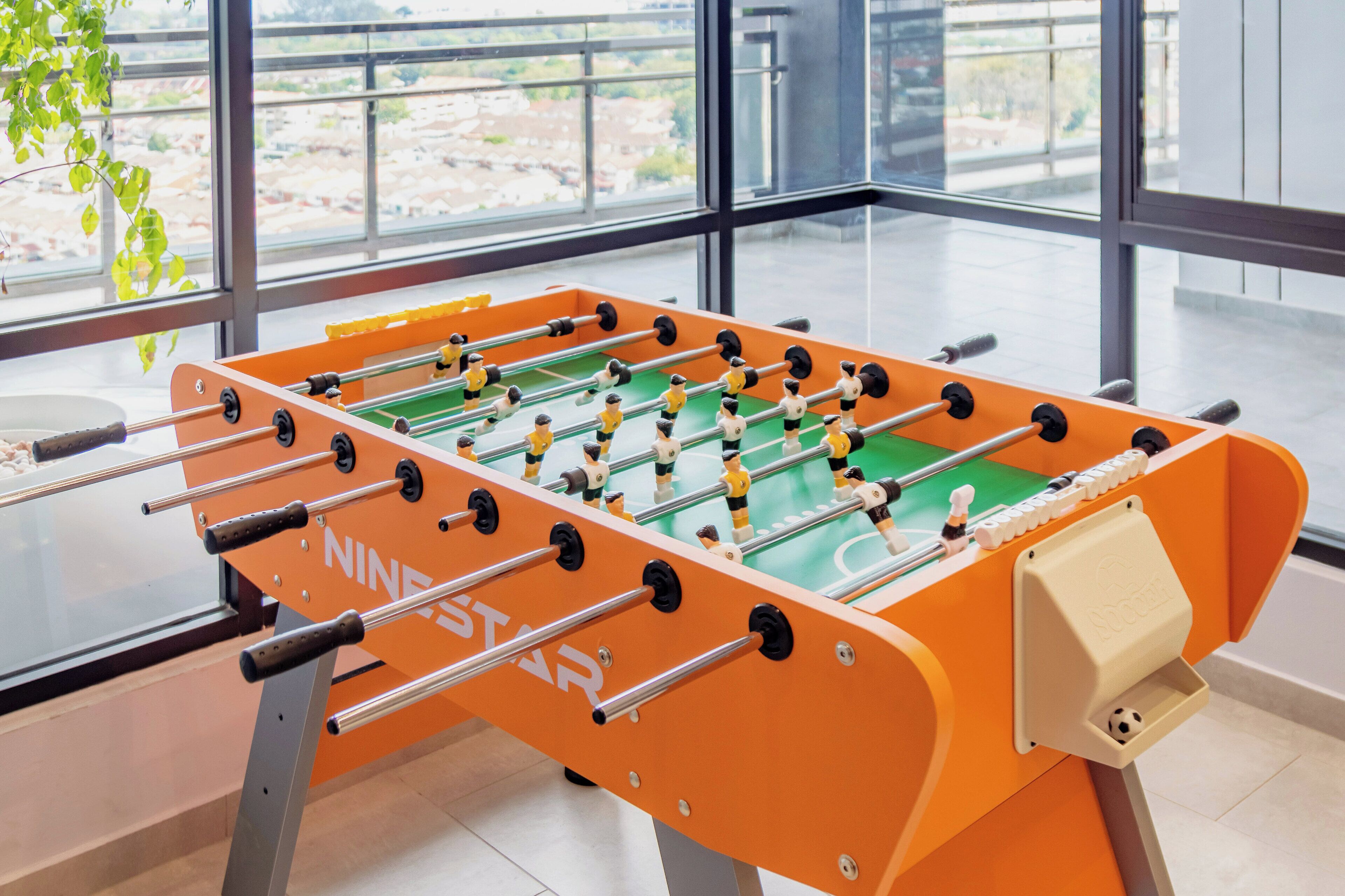 A foosball table with a clear view of the surrounding area through large windows.