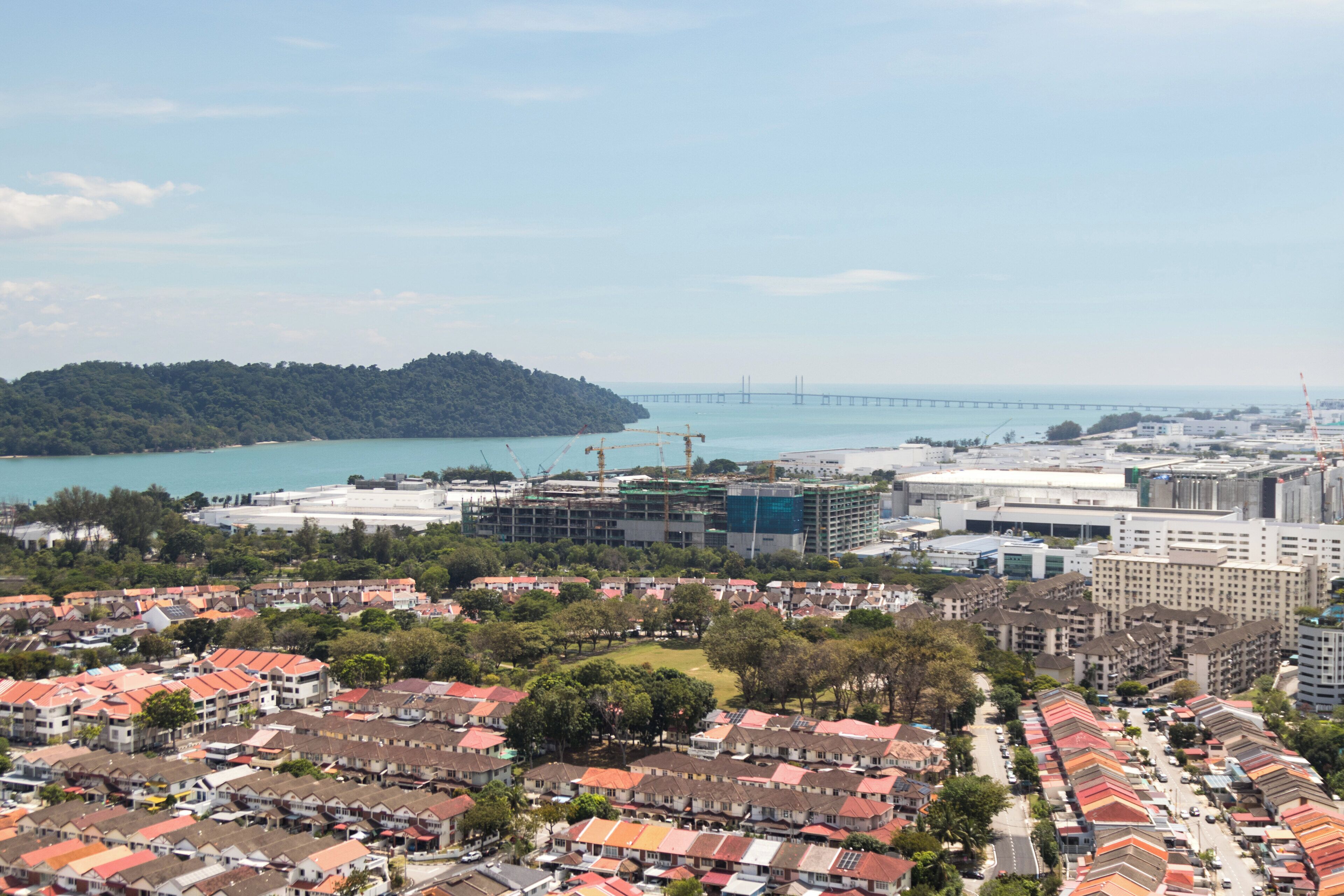 A coastal cityscape with residential buildings, a bridge, and a forested island.