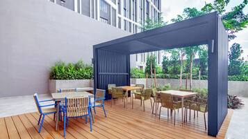 An outdoor patio with wooden flooring, a covered seating area, and a view of a modern building.