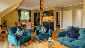 A modern living room with teal armchairs, a wooden coffee table, and a dining area with a bench. - Hünzinger Dorfschmiede - Holiday apartment Zaunkönig (Walsrode)