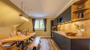 A modern kitchen with wooden cabinetry, a dining table with benches, and a hanging light fixture. - Hünzinger Dorfschmiede - Holiday apartment Zaunkönig (Walsrode)