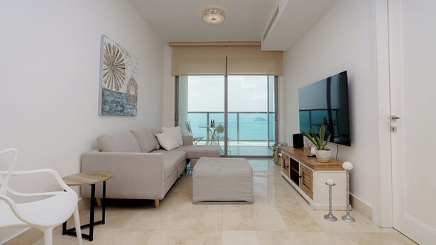 A modern living room with a sofa, a coffee table, a TV, and a balcony with a view of the sea. - Exclusive and luxury 1BR with balcony in Yoo Panama (Panamá)
