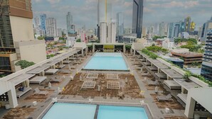 A rooftop pool area with multiple pools and lounge chairs, surrounded by high-rise buildings. - Exclusive and luxury 1BR with balcony in Yoo Panama (Panamá)