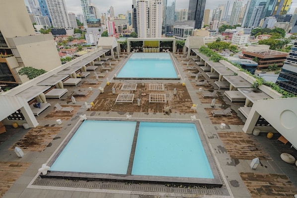 A rooftop pool area with two pools, lounge chairs, and a cityscape view.