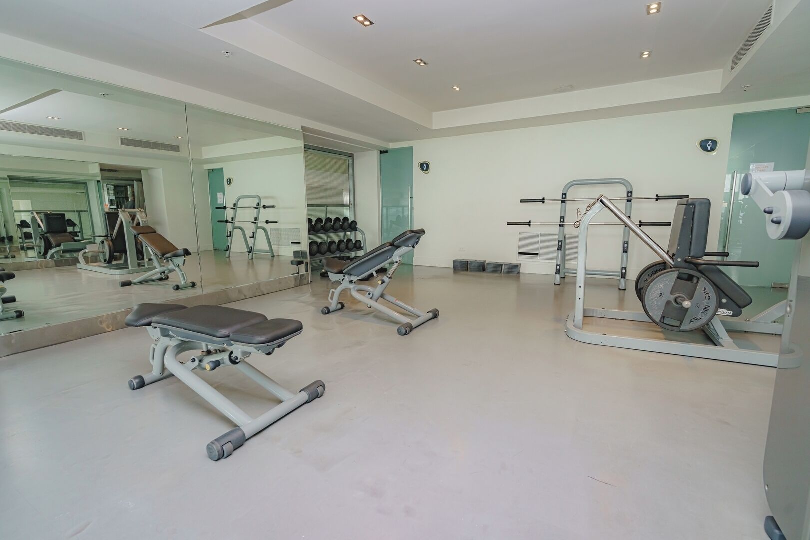 Une salle de sport équipée de matériel d’exercice, d’un banc et d’un mur recouvert de miroirs.