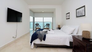 A modern hotel room with a large bed, a flat-screen TV, and a view of the sea through large windows. - Exclusive and luxury 1BR with balcony in Yoo Panama (Panamá)