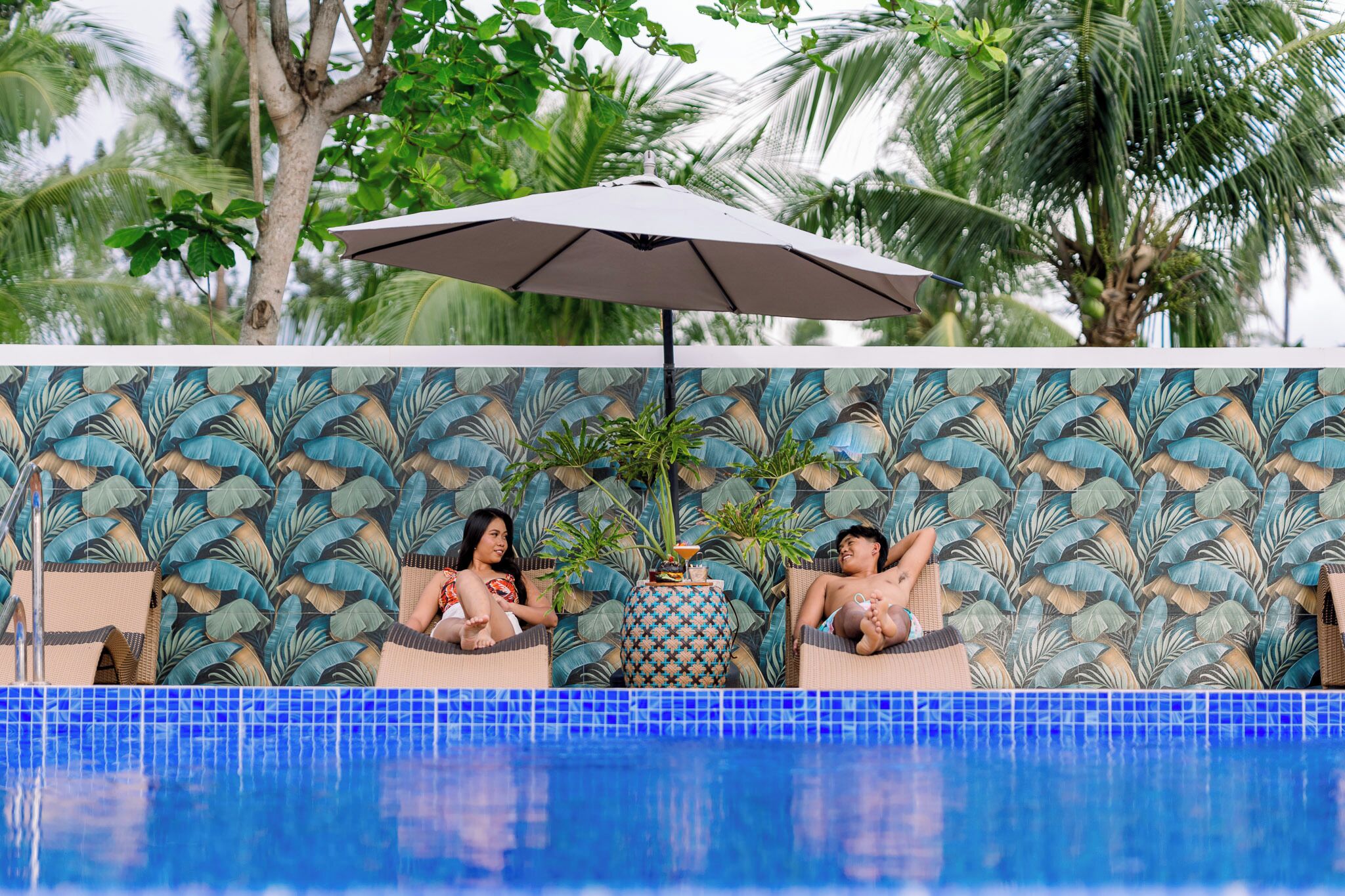 A pool area with two lounge chairs, a patterned wall, and a tiled pool edge.