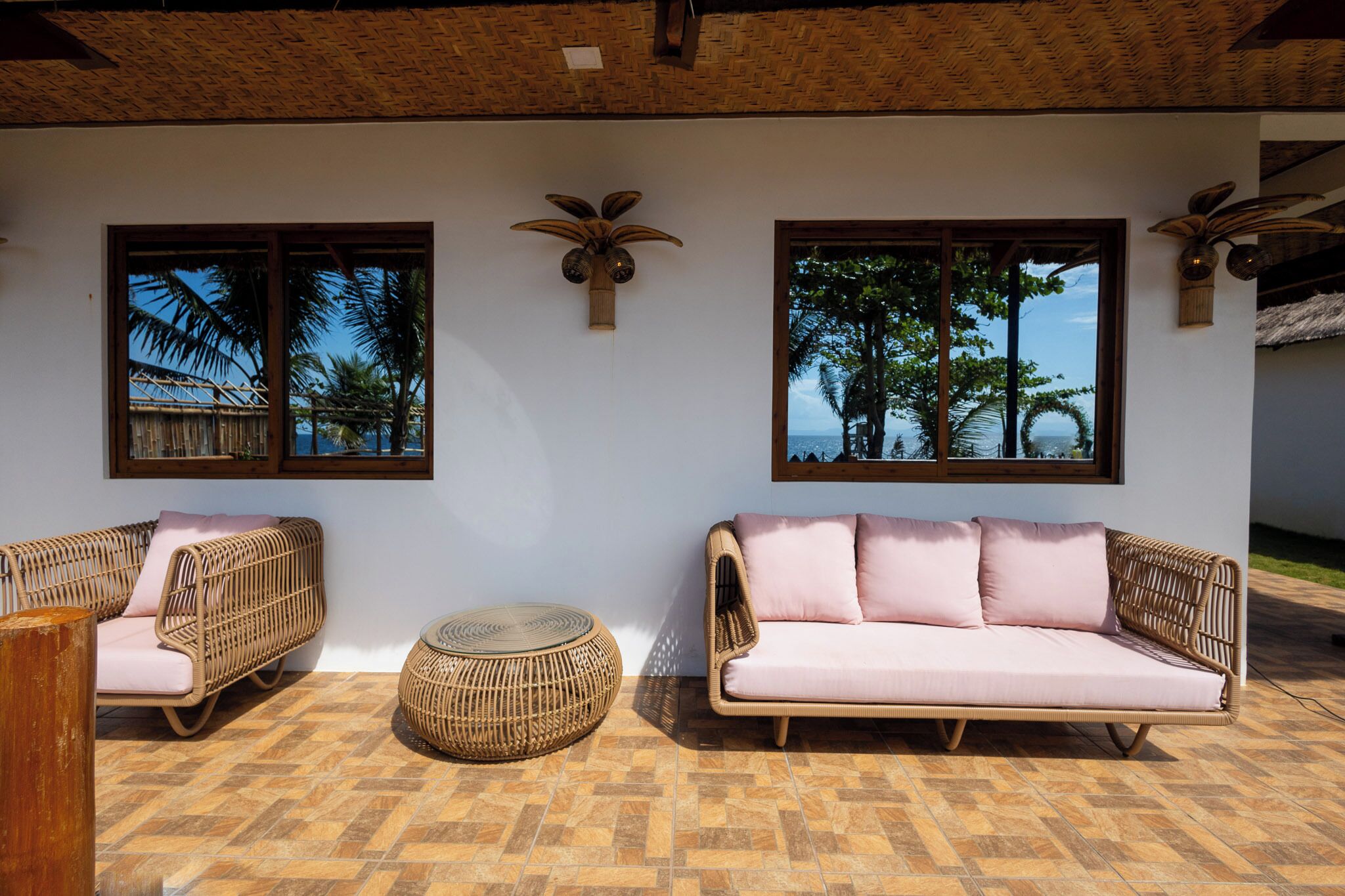 A room with two wicker sofas, a woven ottoman, and two wall-mounted decorative vases.