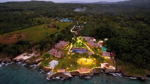 An aerial view of a resort with multiple buildings, a pool, and a beach area surrounded by lush greenery and rocky coastline. - Casa Verde Cliff Resort and Spa (San Francisco)