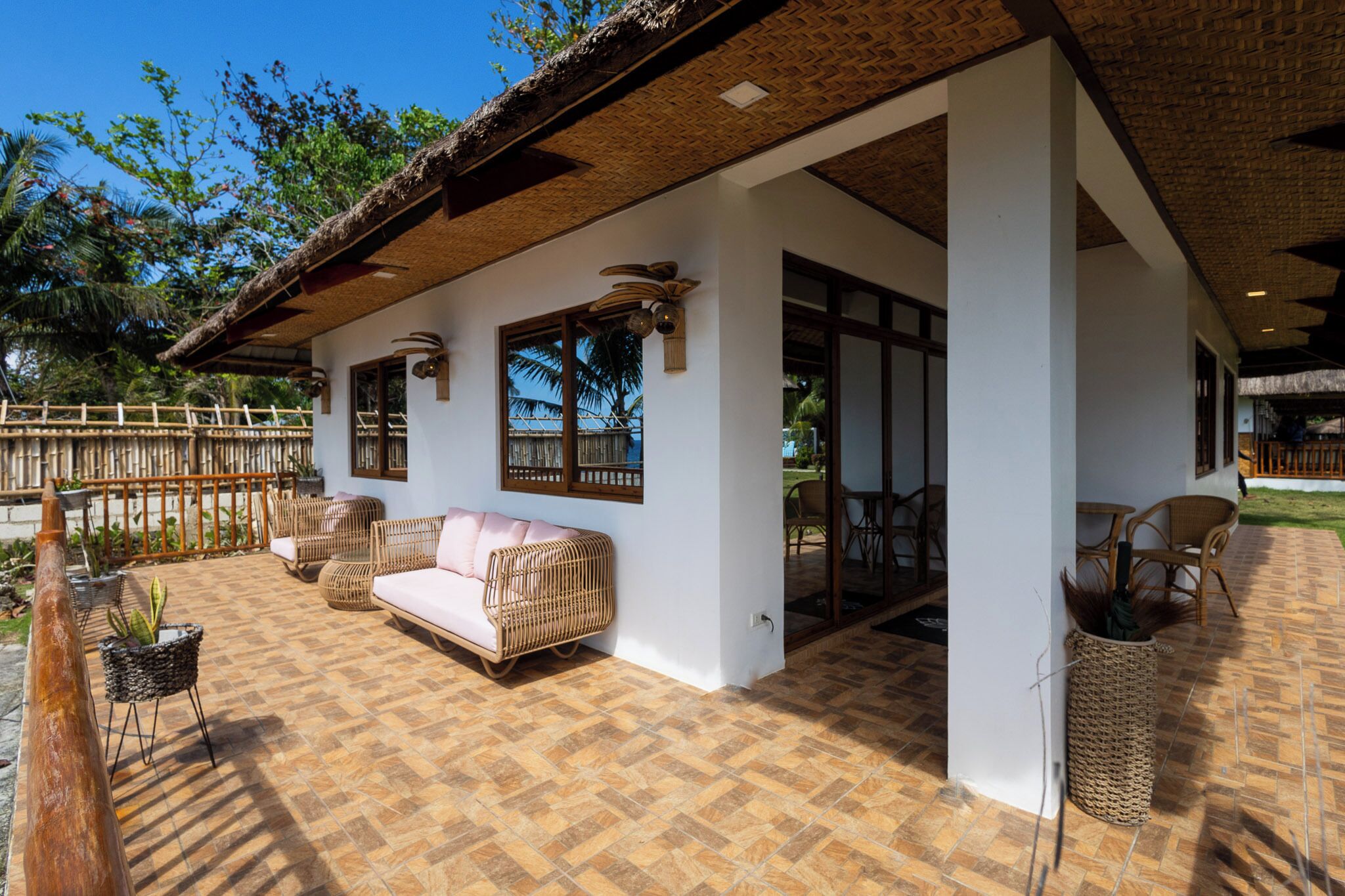 An outdoor patio area with a thatched roof, wicker furniture, and a view of the surrounding landscape.