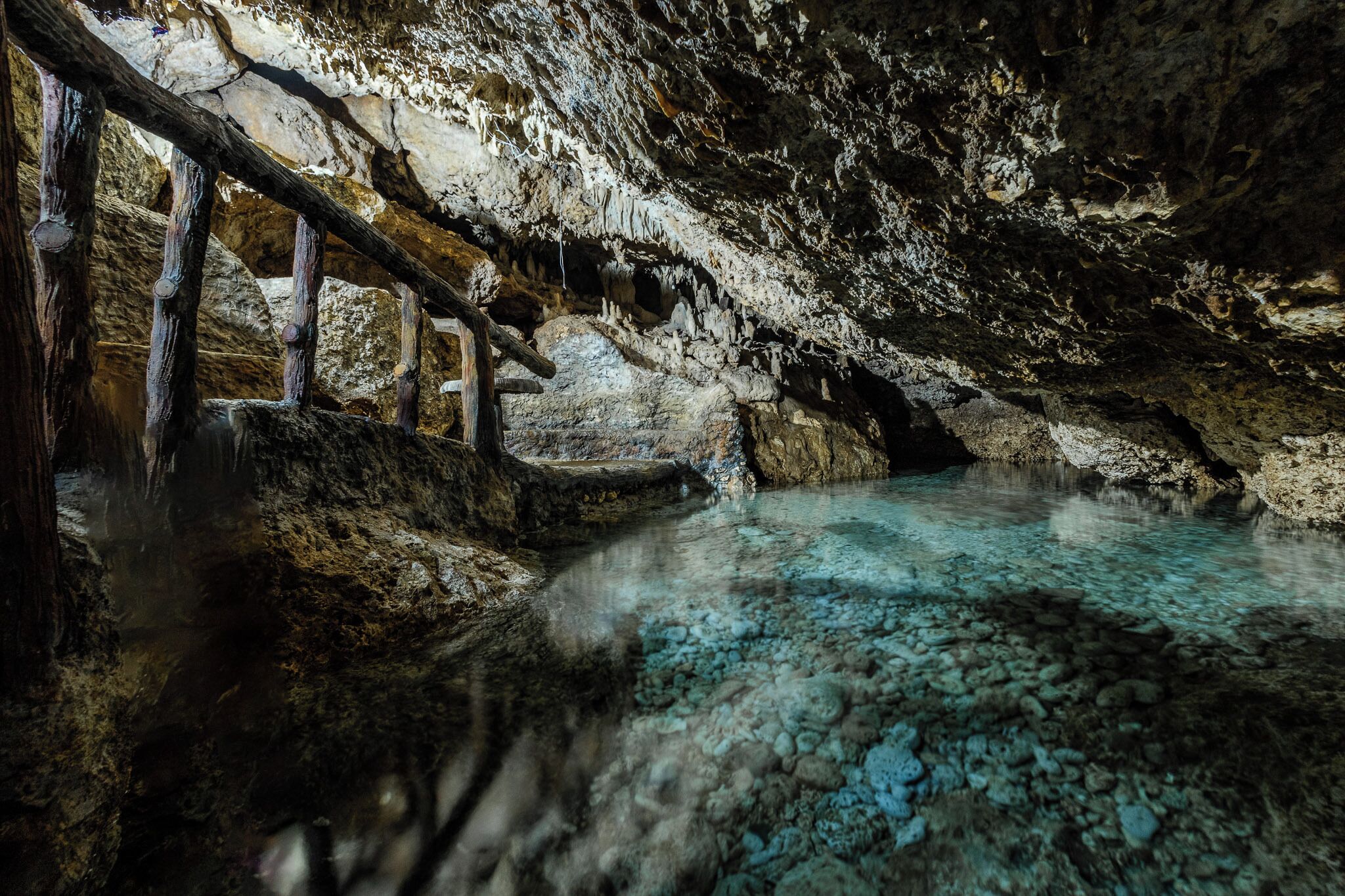 A cave with stalactites, a wooden walkway, and a pool of water.