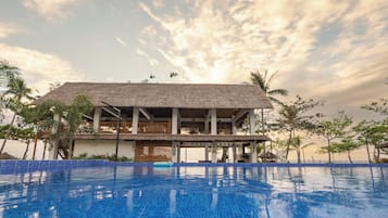 A resort with a large swimming pool, a thatched-roof building, and palm trees.
