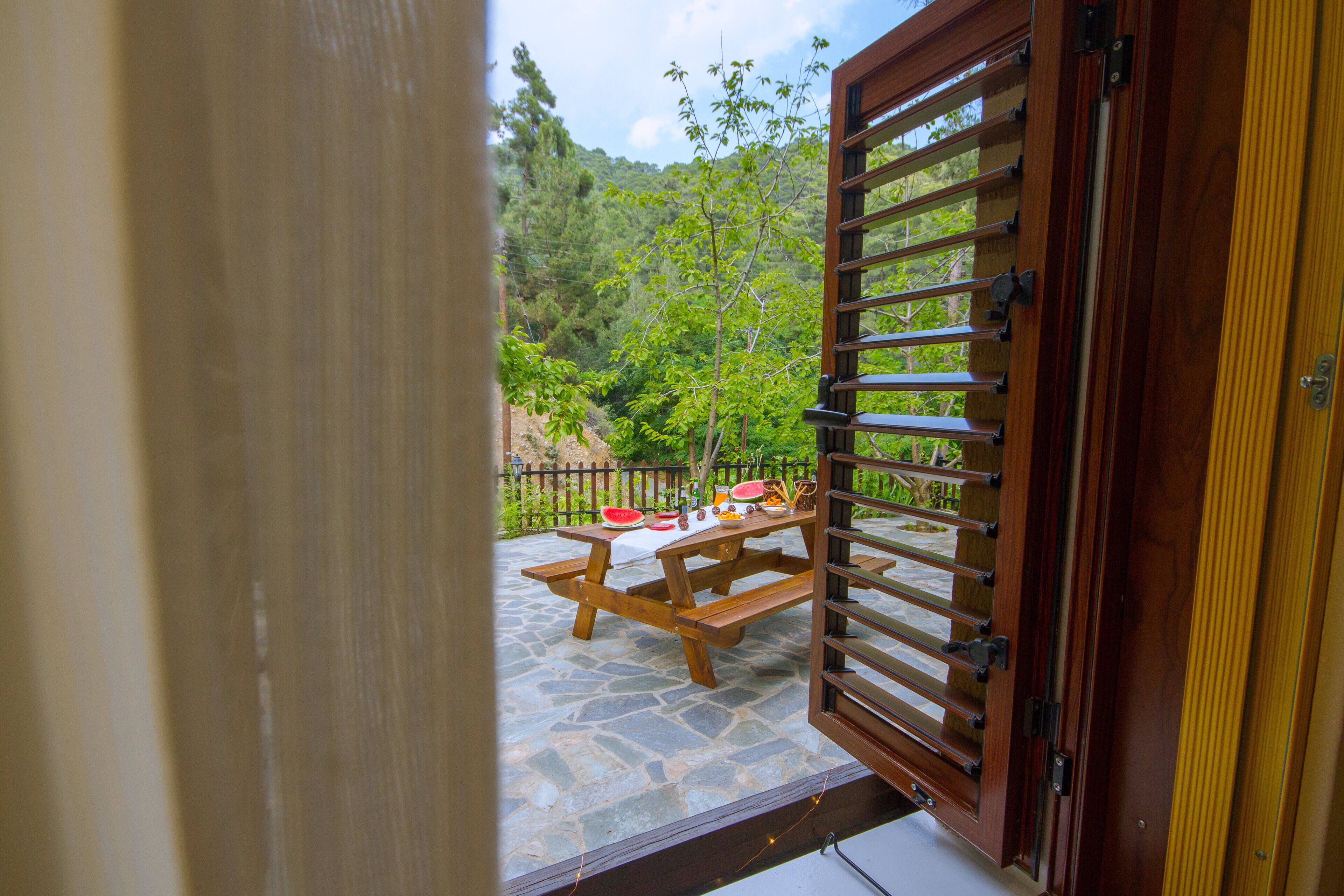 Une porte en bois donnant sur un patio en pierre, avec une table de pique-nique et une pastèque.