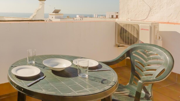 Een eettafel met borden, bestek en glazen op een betegeld terras met uitzicht op zee.