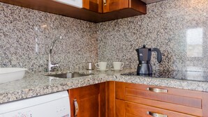 Een keuken met granieten aanrechtbladen, houten kastjes, een roestvrijstalen spoelbak, een koffiezetapparaat en een magnetron.