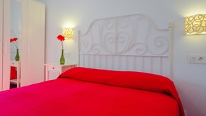 Een slaapkamer met een wit bed, rode beddengoed, een witte kledingkast en twee wandlampen.
