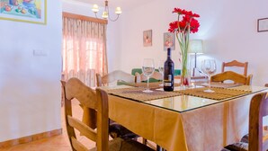 Un comedor con una mesa de vidrio, sillas de madera, una botella de vino y flores rojas.