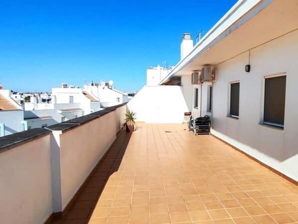 A rooftop terrace with a tiled floor, a potted plant, and a small seating area. - Blue Atlantic Penthouse (Conil de la Frontera)