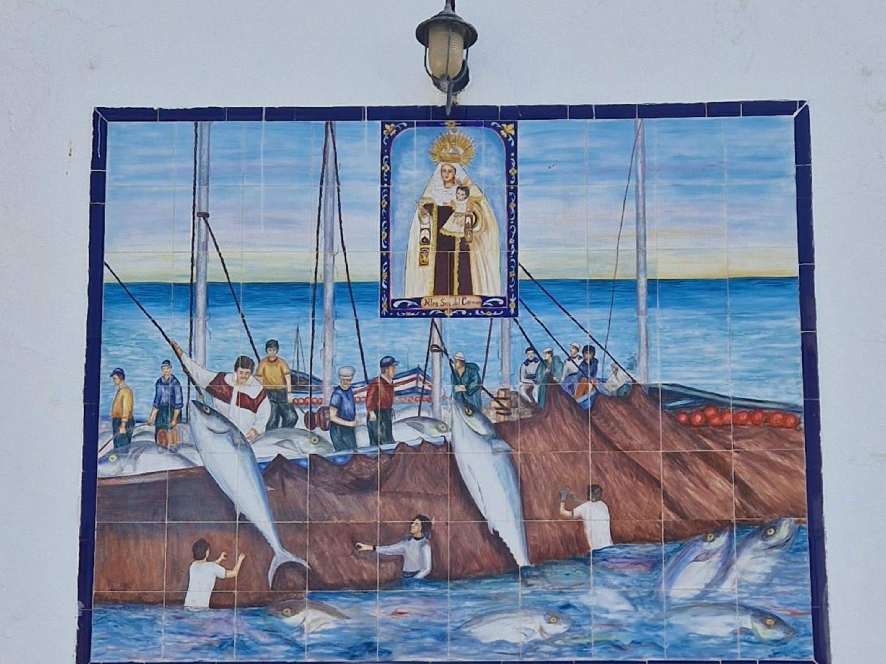 A tiled mural depicting a fishing scene with a boat, people, and a figure of a woman with a child.