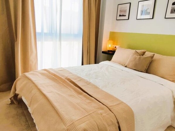 A neatly made bed with a beige and white duvet, a bedside table with a lamp, and a wall with framed pictures. - Smart Conil los Bateles 28584 (Conil de la Frontera)