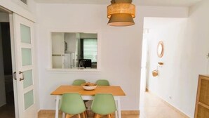 A dining area with a wooden table and green chairs, a hanging light fixture, and a view of a kitchen through a window. - Smart Conil los Bateles 28584 (Conil de la Frontera)