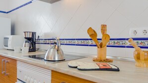 A kitchen with a stove, kettle, coffee maker, and wooden utensils on the counter. - Casa Mariana 1417 in Conil de la Frontera (Conil de la Frontera)
