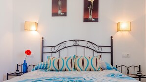 A neatly made bed with patterned pillows, a blue vase with a red flower, and two wall-mounted lamps. - Casa Mariana 1417 in Conil de la Frontera (Conil de la Frontera)