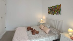 Un dormitorio con cama, mesitas de noche, ventilador de techo y una obra de arte en la pared.