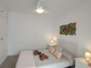 Ein Schlafzimmer mit Bett, Nachttischen, Deckenventilator und einem Wandbild.