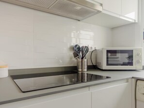A modern kitchen with white cabinets, a black induction cooktop, and a white microwave.