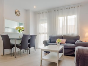 Una sala de estar moderna con un sofá gris, una mesa de centro blanca y un comedor con una mesa de vidrio y sillas.