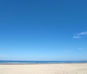 Ein weiter, sandiger Strand mit blauem, klarem Himmel.