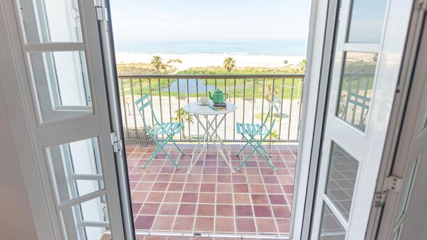 A balcony with a view of the ocean, a table with chairs, and a green kettle. - Balc n Atl Ntico 27786 (Conil de la Frontera)