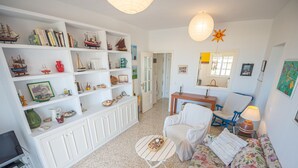 A cozy living room with a white sofa, two white armchairs, a coffee table, and a bookshelf filled with books and decorative items. - Balc n Atl Ntico 27786 (Conil de la Frontera)