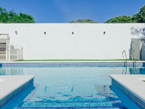 A swimming pool with clear blue water, surrounded by a white wall and a green lawn. - Moon Villa in Conil de la Frontera (Conil de la Frontera)