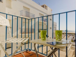 A balcony with a white chair, a small table, and two green vases. - Apartamento Carril de la Fuente 17597 (Conil de la Frontera)