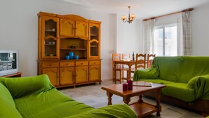 Ein Wohnzimmer mit Holzschrank, grünen Sofas, einem Holztisch und einem Esstisch mit Stühlen.