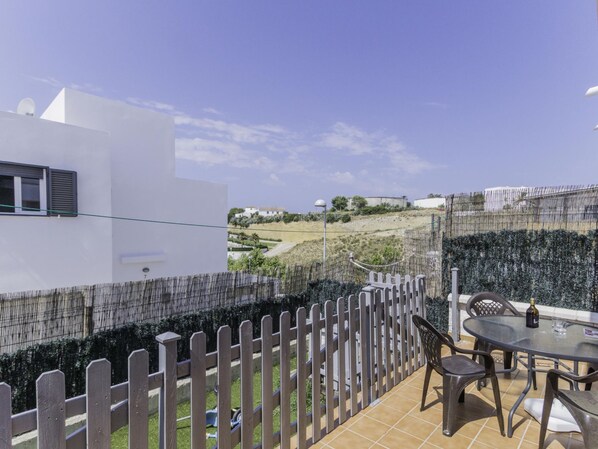 Un patio con una mesa y sillas, una cerca y vistas a un paisaje montañoso.