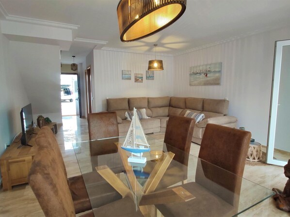 A modern living room with a glass coffee table, brown leather chairs, a beige sectional sofa, and a hanging pendant light. - Villa Libertad 10409 (Conil de la Frontera)