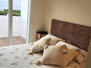 A bedroom with a bed, two pillows, a nightstand, and a view of a balcony. - Villa Libertad 10409 (Conil de la Frontera)