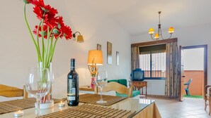Comedor con una mesa lista para dos personas, que incluye una botella de vino, copas y un jarrón con flores rojas.