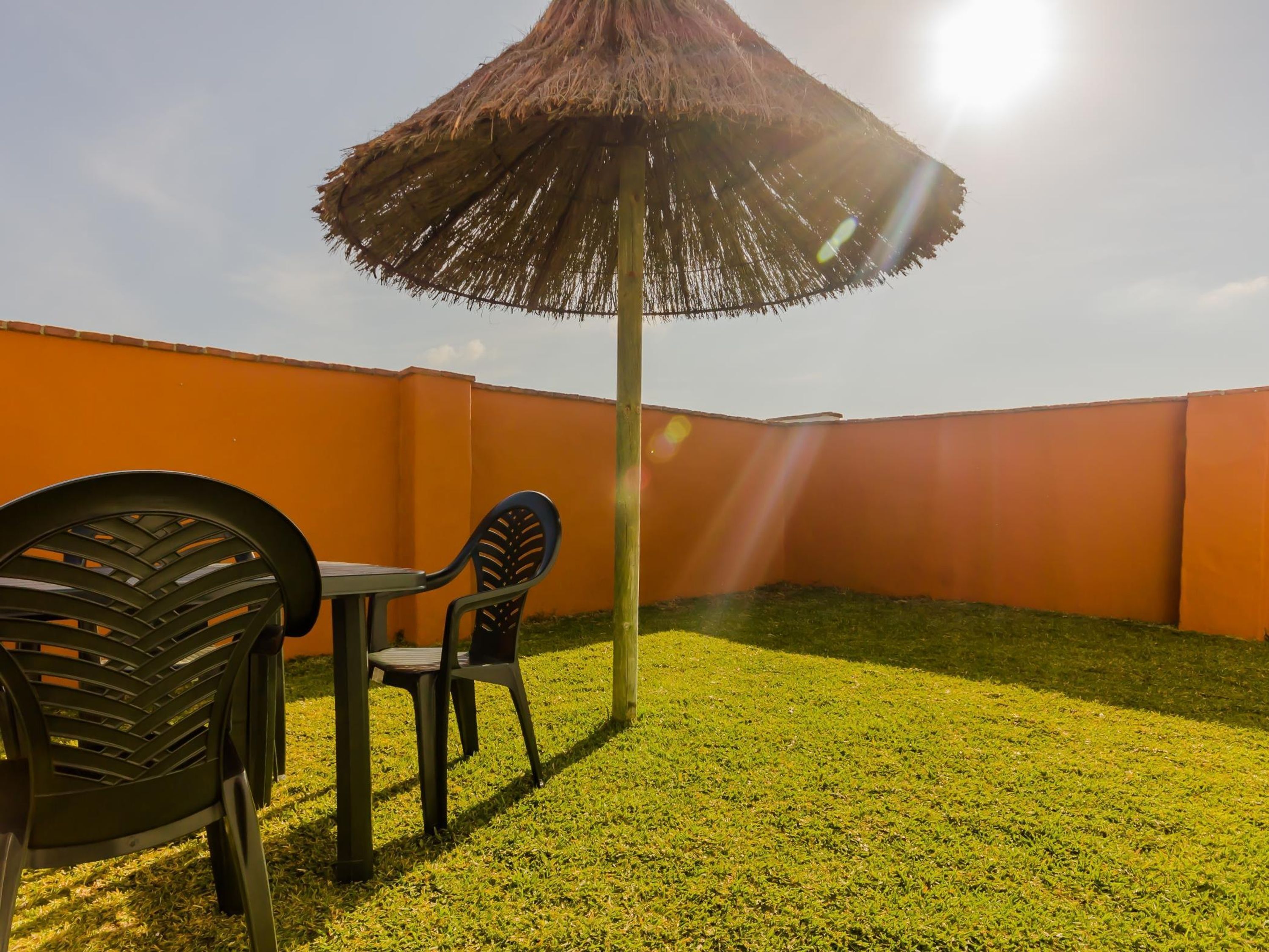 Un patio con un ombrellone di paglia, due sedie e un tavolo.